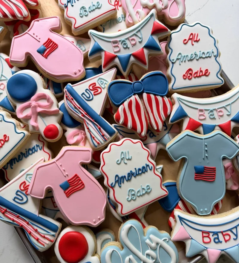 Red, white, and blue baby shower cookies with flags and onesies.