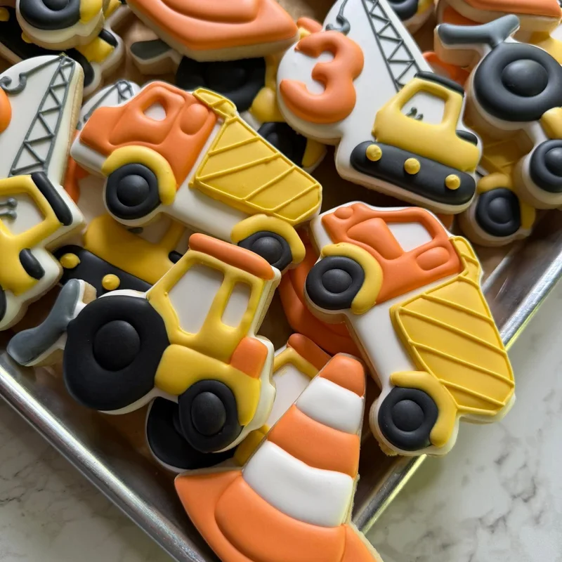 Dump truck and crane cookies in orange and yellow, with the number three.