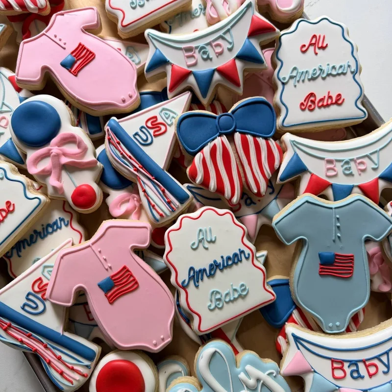 Red, white, and blue baby shower cookies with flags and onesies.