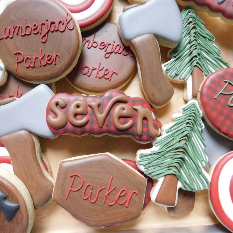 Lumberjack-themed cookies with axes, plaid, pine trees, and the word seven.